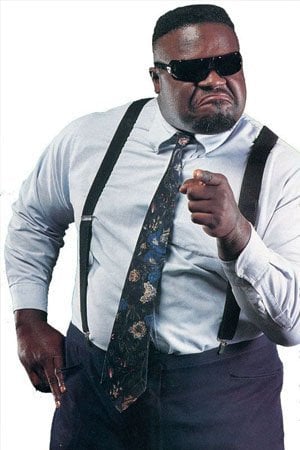 Pro wrestling is a self-contained community that roams place to place with squabbles quickly resolved and forgotten - unless you're with Mr Hughes! Mr Hughes in a suit and black sunglasses pointing outward