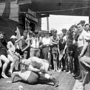 Carnival wrestling match in progress (circa late 1800s): Wrestlers grappling while spectators gather to witness the athletic show. This format became the foundation for all professional wrestling exhibitions across America. The “worked” nature of these matches, combining legitimate holds with predetermined outcomes, established the entertainment model that professional wrestling still uses today.