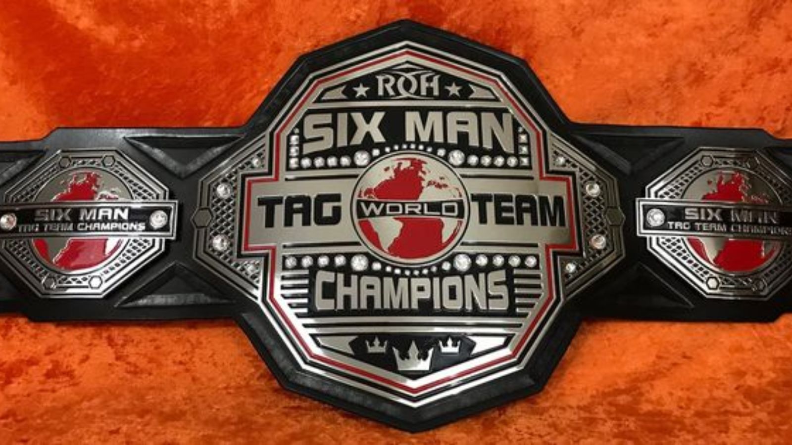 The ROH World Six-Man Tag Team Championship second design was introduced in 2018 and first held by The Kingdom in 2016. It features a sleek black strap and silver plates with a bold red globe centerpiece.