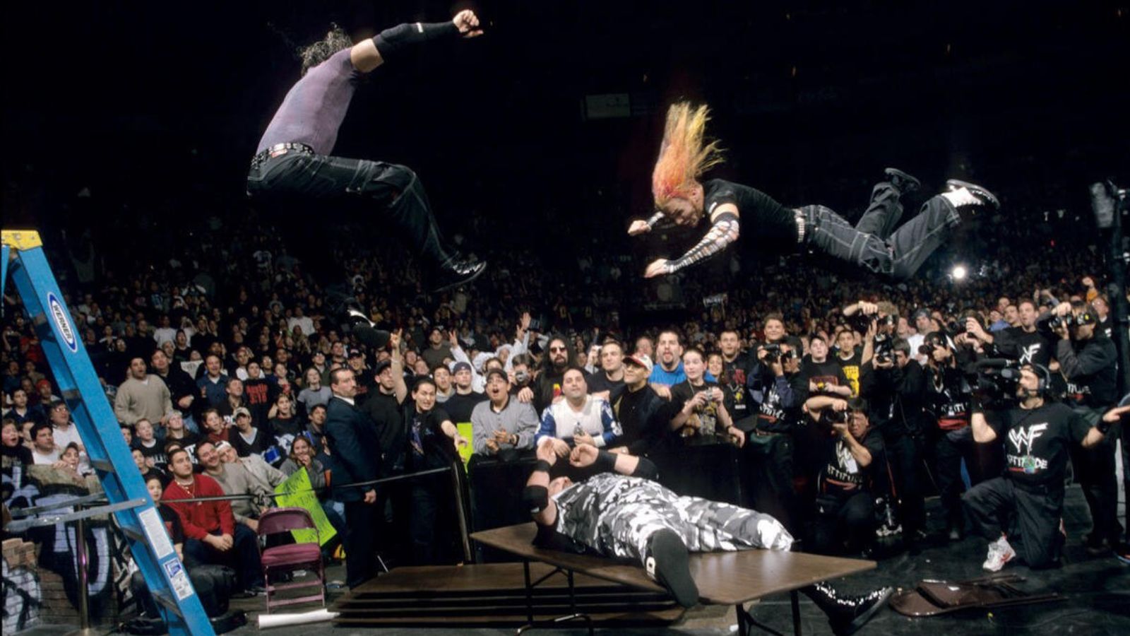 Royal Rumble 2000: The Hardy Boyz target Bubba Ray Dudley seated on a ringside table. Matt Hardy hits a leg drop, then Jeff Hardy follows with a Swanton Splash (Event Omega) – burying Bubba through the table. 