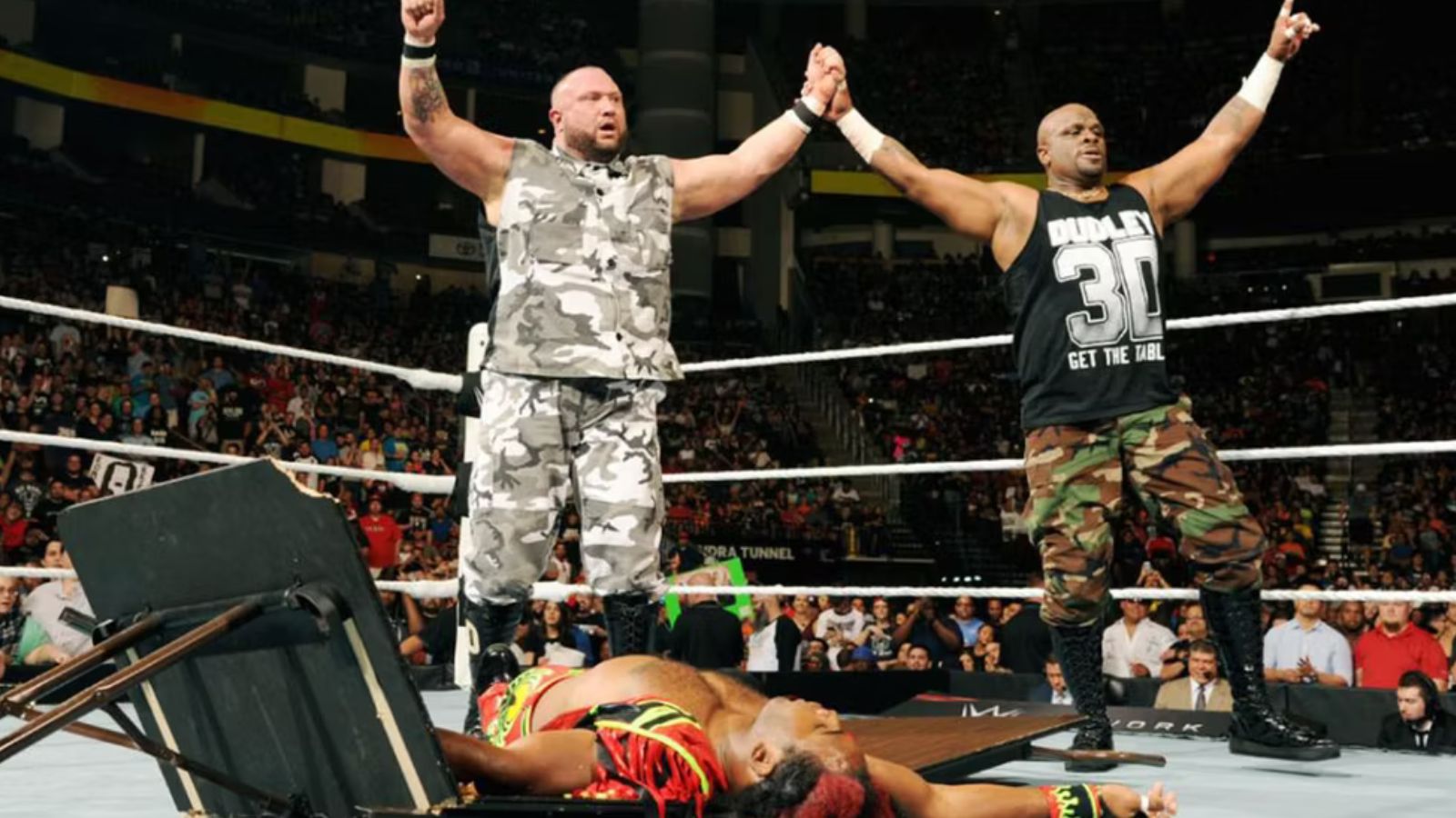 Post-match scene: The Dudley Boyz (Bubba Ray & D-Von) celebrate after putting both New Day members through tables. In WWE, Bubba famously shouts ‘D-Von, get the tables!’ to signal this devastating finale. 