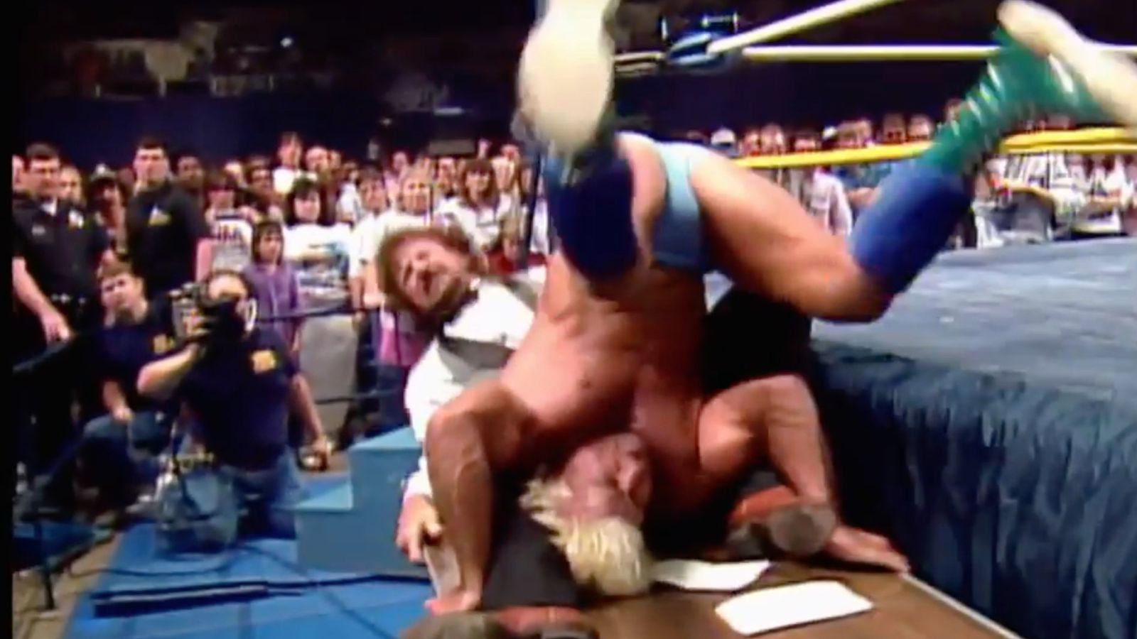Wrestle War ’89: NWA champion Ric Flair is sitting on a table ringside as Terry Funk runs in with a surprise piledriver. Both crash through the hardwood in an unplanned historic spot. 