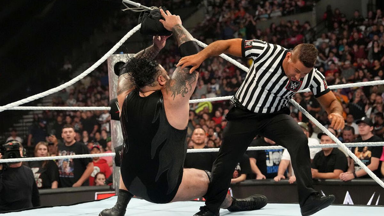 Bronson Reed removes a turnbuckle pad as part of a planned sequence, sending himself to the mat and unbalancing WWE wrestling referee Danilo Anfibio, who, as the official, will soon clear away hazards. 