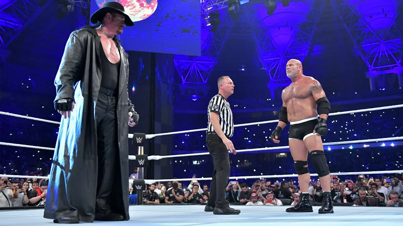 WWE wrestling referee Mike Chioda stands between The Undertaker and Bill Goldberg before their only singles match at Super ShowDown on June 7, 2019, in Jeddah, Saudi Arabia. 