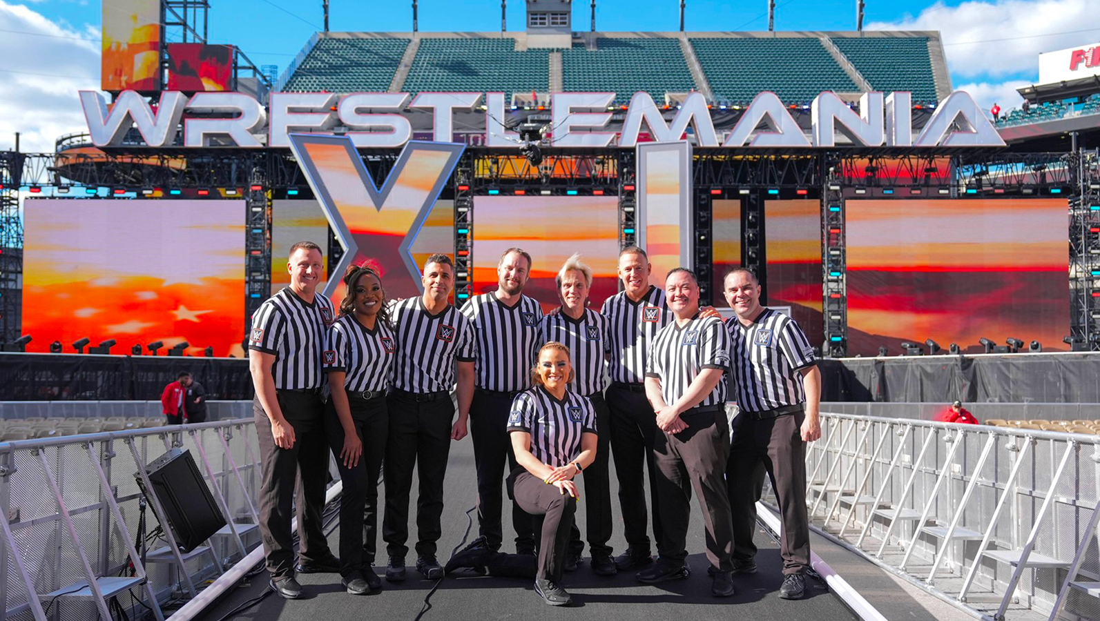 WWE referee team at WrestleMania 40 on April 6-7, 2024, in Philadelphia: Shawn Bennett, Daphanie LaShaunn, Eddie Orengo, Jason Ayers, Jessika Carr (front-center), Charles Robinson, Chad Patton, Ryan Tran, and Dan Engler – standing ready behind the scenes amid larger-than-life personas of the wrestlers. 
