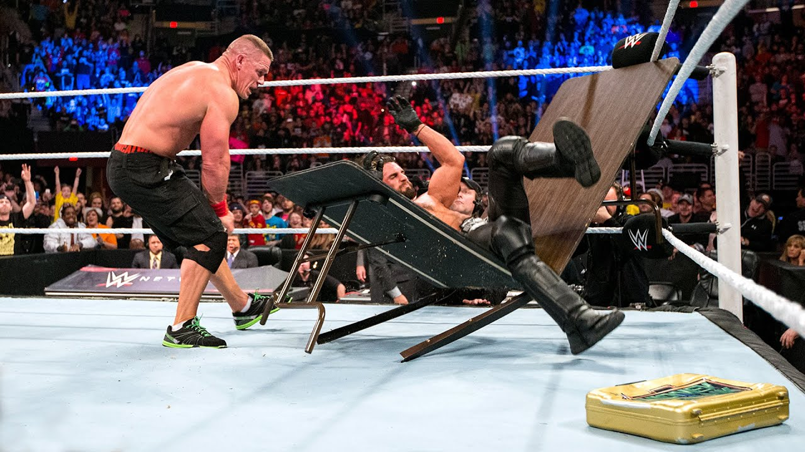 WWE Superstars John Cena and Seth Rollins collide at TLC 2014. Cena powers Rollins through a propped-up ringside table with his Attitude Adjustment.