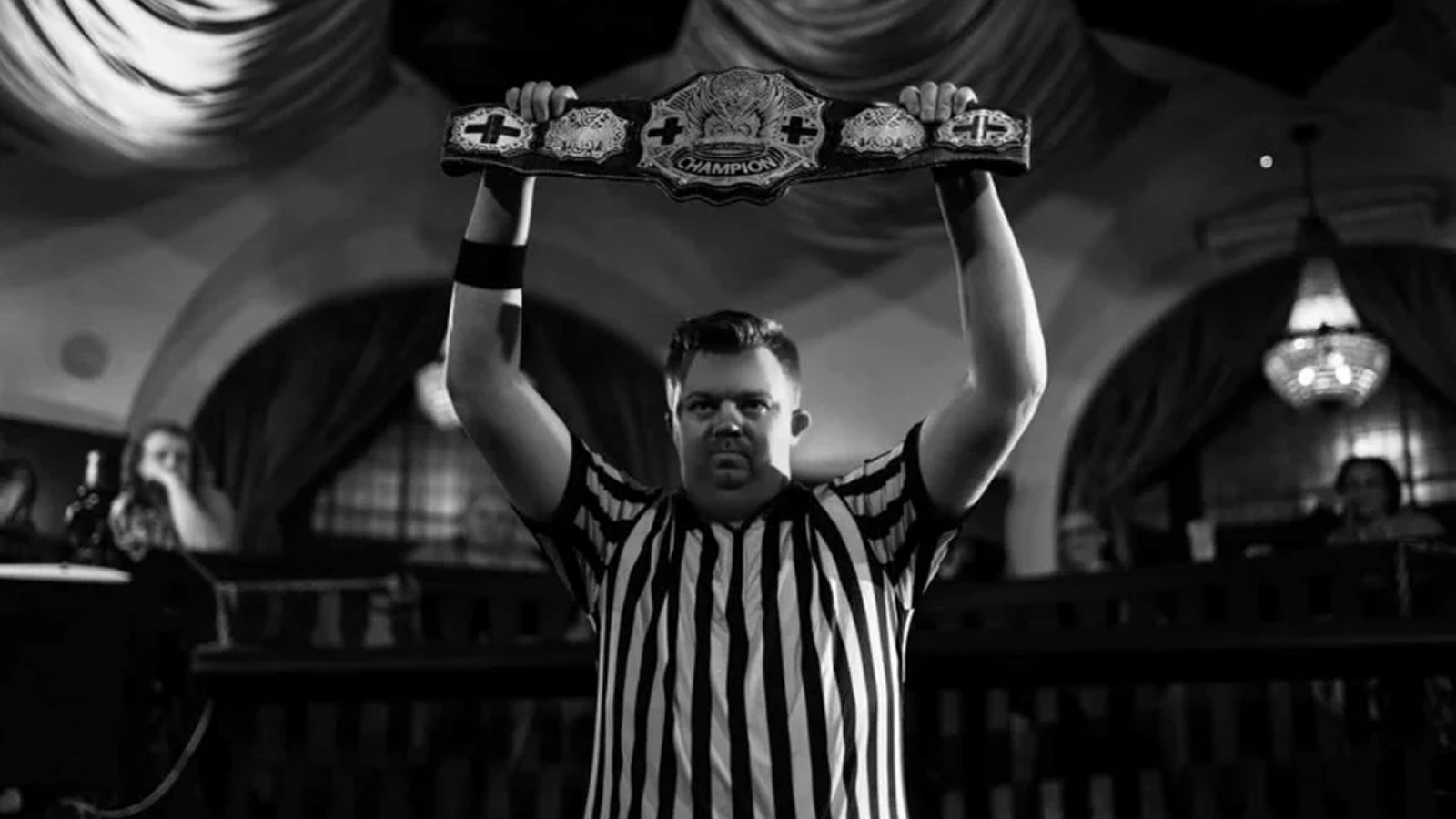 Independent wrestling referee Josh Wallis hoists a championship belt up high before an indie show match. As Wallis shared with Pro Wrestling Stories, wrestling referees don’t just enforce rules – they elevate match quality, ensure wrestler safety, and orchestrate seamless storytelling from the squared circle’s center. 