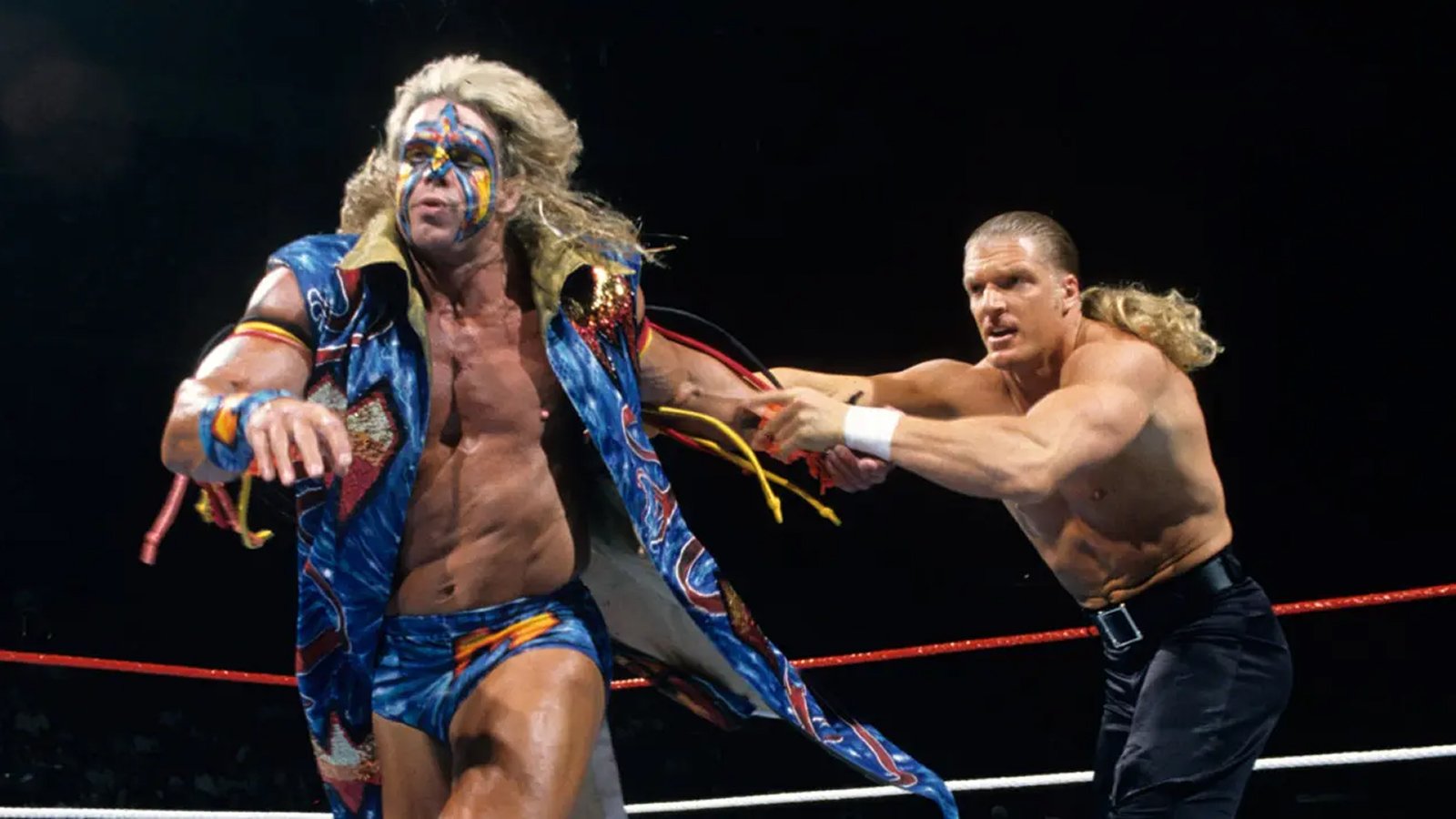 Triple H sends the Ultimate Warrior up against the ropes in their infamous encounter at WrestleMania XII where the Warrior soundly defeated Triple H in a matter of a few seconds, kicking out of the Pedigree and delivering an onslaught of offence in his return.