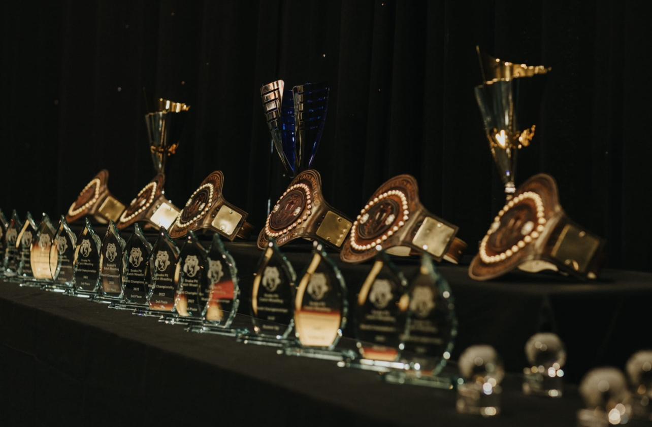 Championship belts and wrestling memorabilia preserved at the Snake Pit gymnasium, representing seven decades of catch wrestling excellence spanning from Billy Riley’s era through Roy Wood’s stewardship to present day. 