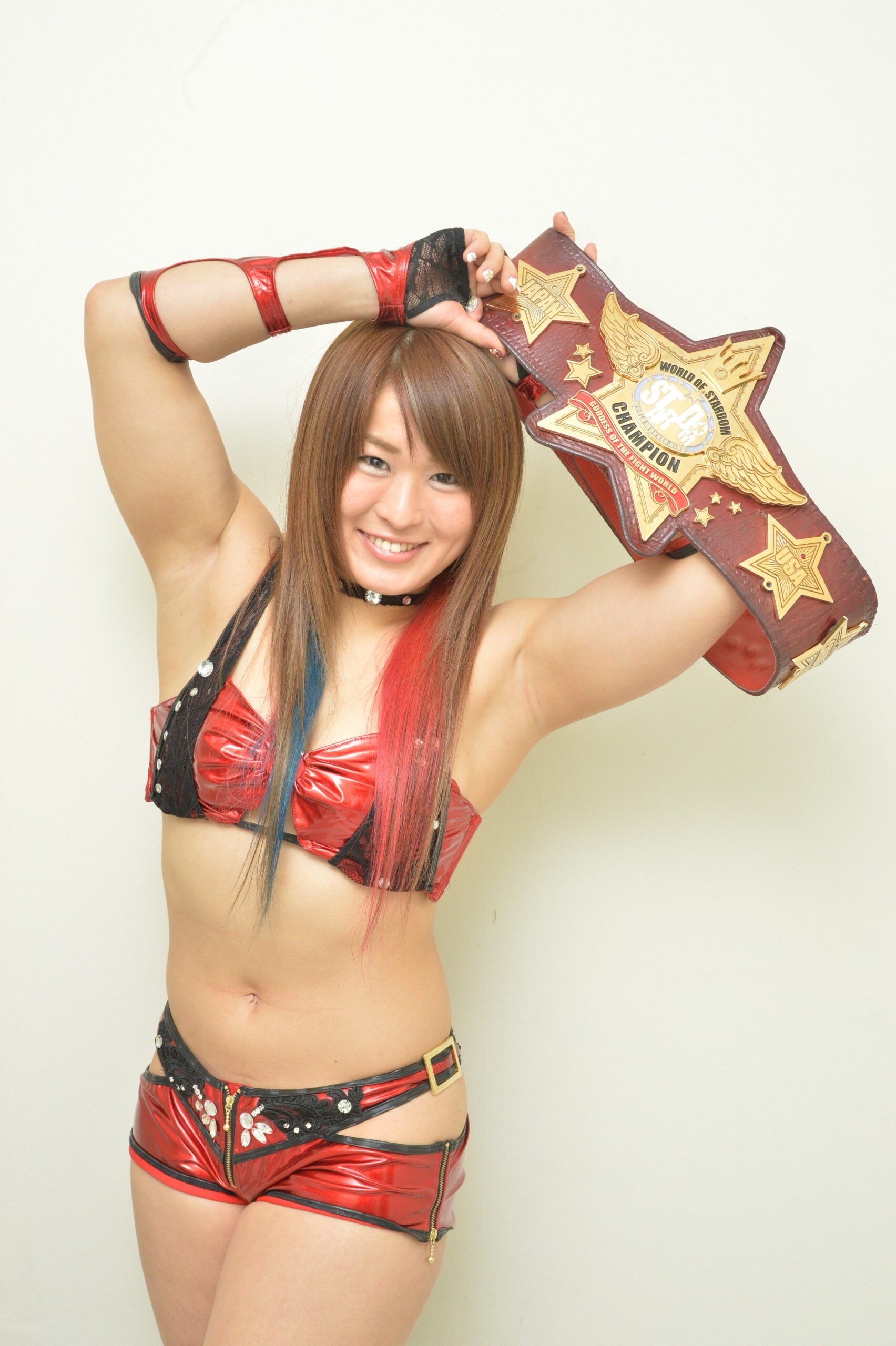 Io Shirai (WWE's IYO SKY) pictured in 2016 as the World of Stardom Champion, proudly holding the prestigious Red Belt, the top Japanese women's title in professional wrestling. By this moment, she had rebuilt her career from the wreckage of the 2012 Narita Airport incident that nearly ended everything. This image captures not just a championship reign, but a triumph over conspiracy, false accusation, and the resilience it took to reclaim her place among wrestling's elite. 