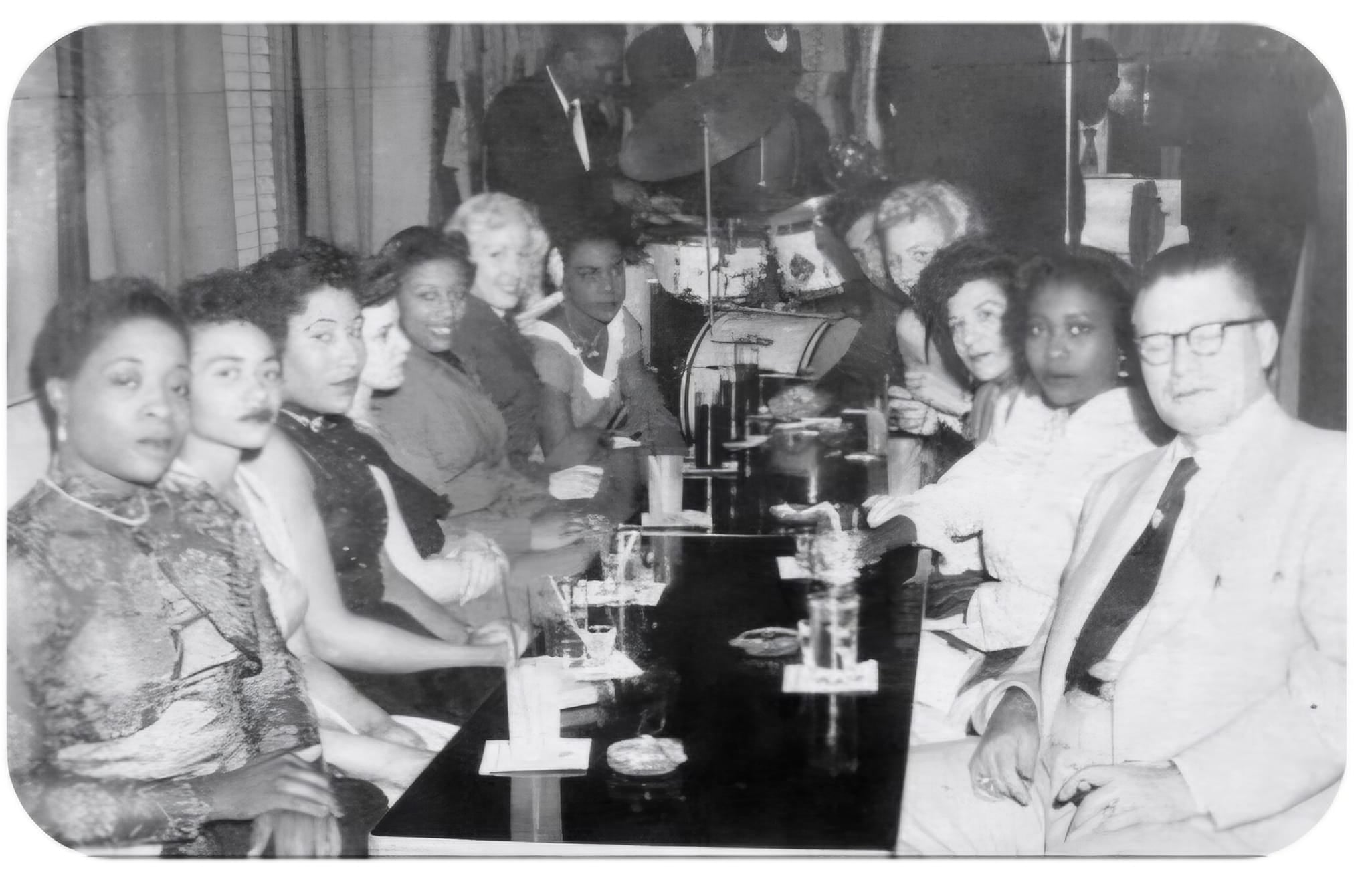 Billy Wolfe pictured with members of his women’s wrestling troupe, the integrated group of Black and white women whose careers meant constant travel through a deeply segregated America. For the Black wrestlers among them, pioneers like Ethel Johnson, Babs Wingo, Marva Scott, Louise Greene, Betty White, Kathleen Wimbley, Lula Mae Provo, Mary Horton, and Dinah Beamon, every booking could mean hours of night driving for a single meal, lodging in private guest houses when hotels turned them away, and entering buildings where the law itself stood against them. 