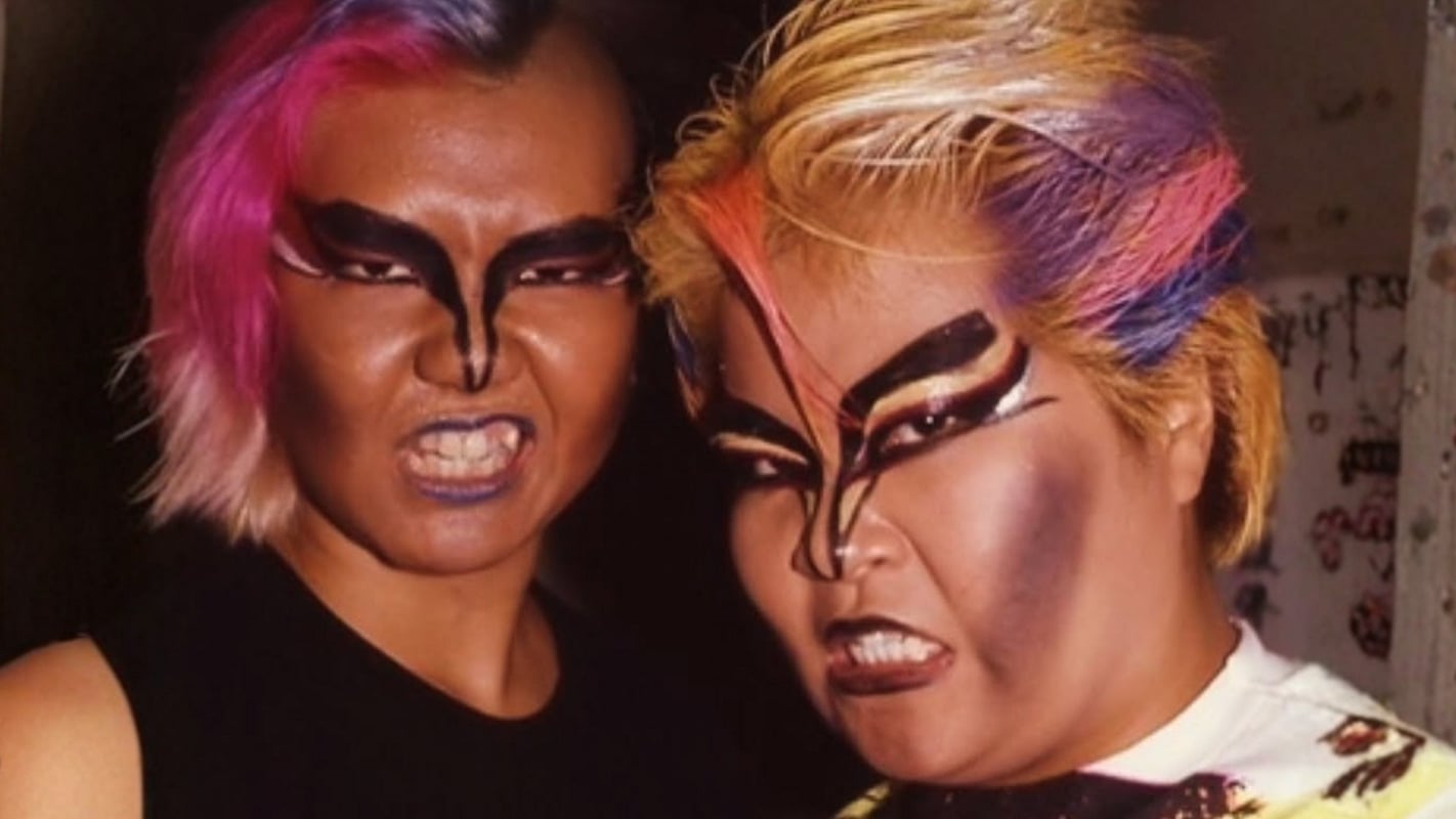 Dump Matsumoto and Bull Nakano of the Gokuaku Domei (Atrocious Alliance) in full character: bleached and teased hair, and theatrical face paint, a look drawn from KISS-inspired glam-rock excess and sukeban delinquent culture that made them the most visually striking and feared heels in 1980s All Japan Women's Pro-Wrestling (AJW). 
